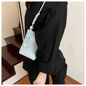 Detail of light blue PU bucket bag with braided strap, pearl accent, and bow label detail