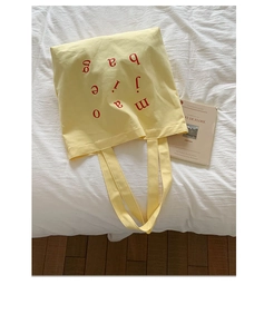 Macro shot of yellow canvas tote bag featuring red artistic font and shoulder strap detail