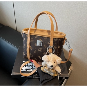 Détail d'un sac à main marron foncé avec motifs d'ours et un pendentif ours en peluche