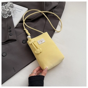 Detail of a bright yellow crossbody phone bag featuring a white pearl and heart charms
