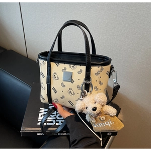 Détail d'un sac cabas crème avec motifs d'ours, bordure noire et breloque ours en peluche