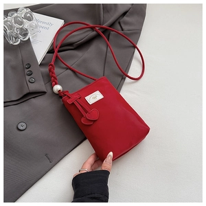 Detail of red PU phone bag with pearl strap, bow logo and heart-shaped charms