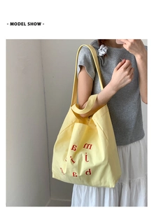 Model wearing a large yellow canvas tote bag with red artistic letter print