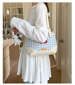 Detail of blue plaid shoulder bag featuring a heart patch and plush rabbit charm