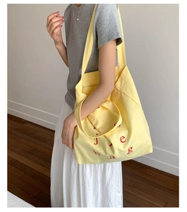 Detailed shot of yellow canvas tote bag featuring red letter patterns and dual strap handles