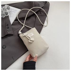 Detail of off-white PU phone bag with pearl strap accent and heart charm on grey jacket