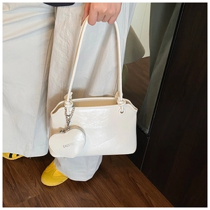 Detail of a creamy white underarm bag with a heart-shaped charm and knot shoulder strap