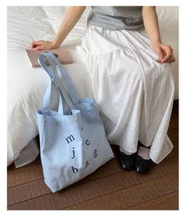 Detail shot of light blue canvas tote bag featuring black lettering in a cozy setting