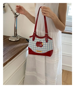 Close-up of blue gingham shoulder bag with red apple patch and shiny leather strap