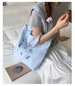 Lifestyle shot of light blue canvas tote bag with black letters on a minimal white bed
