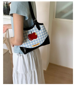 Detail view of canvas blue checkered tote bag with red apple patch on shoulder model