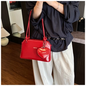 Detail of red patent leather shoulder bag with glossy finish and heart charm