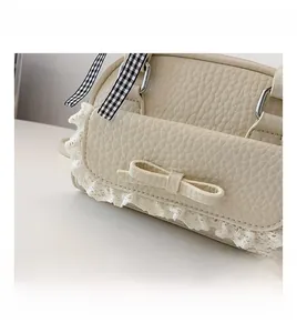 Close-up of cream textured leather bag with white lace trim and a delicate bow detail