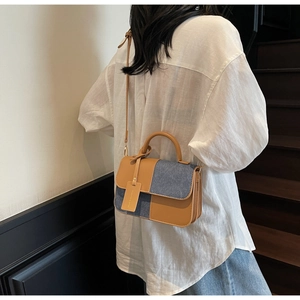 Detail shot of blue denim and brown leather patchwork crossbody bag worn by a model