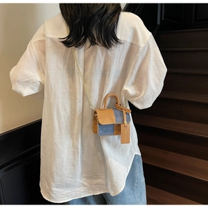 Detail of a mini denim and brown leather contrast crossbody bag with gold chain strap