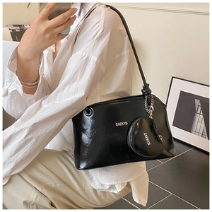 Close-up of black glossy leather underarm bag with white logo and heart charm detail