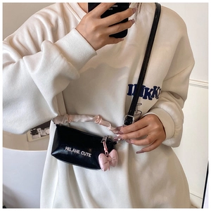Détail du mini sac bandoulière noir avec anse en soie rose et pendentif nœud