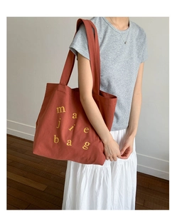 Detail of caramel canvas tote bag with yellow letters shown on model in minimalist room