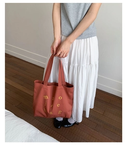 Close-up of brick red canvas tote bag with yellow letters styled on a fashion model