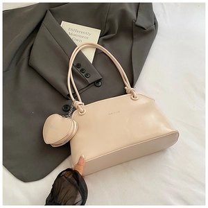 Close-up of a cream underarm bag featuring a small heart-shaped charm and logo detail