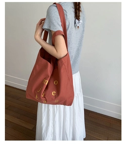 Detail view of large brick red canvas tote bag with yellow artistic lettering and dual straps