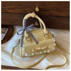 Close-up of shell bag featuring white lace pocket, leather bow, and plaid ribbon detail