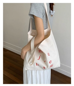 Detail of white canvas tote bag with red letter print and dual handle strap design
