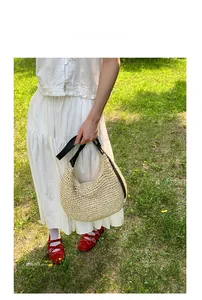 Close-up of woven straw tote bag with black leather strap on outdoor lawn setting