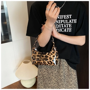 Chic leopard print patent leather handbag held by model in a minimalist home setting