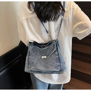 Detail view of denim hobo bag with silver metal swivel lock and chain strap on shoulder