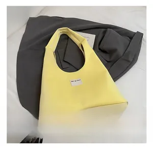 Detail of the light yellow nylon tote bag featuring a minimalist grey rectangular logo tag