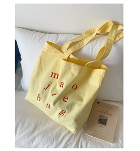 Detailed close-up of thick light yellow canvas texture and red letter print on tote bag