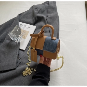 Detail view of the brown leather and blue denim patchwork on the small square bag