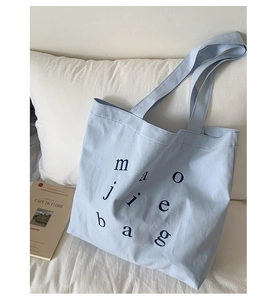 Detail of light blue canvas tote bag on white bedding showing modern graphic typography