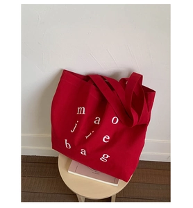 Detail of red canvas tote bag with white lettering on wooden stool with book