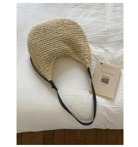 Close-up of oatmeal woven tote bag with black leather strap on white textured bedding