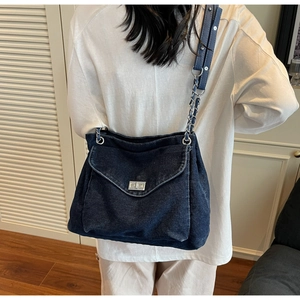 Detail of blue denim tote bag featuring a silver metal rotating lock and chain strap