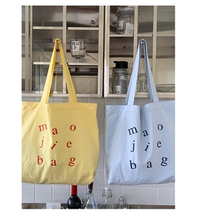 Detail of yellow and light blue canvas tote bags with artistic letter design on a white wall