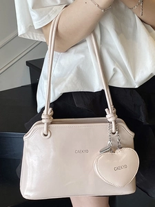 Chic cream leather underarm bag with double handles and heart-shaped charm on stairs