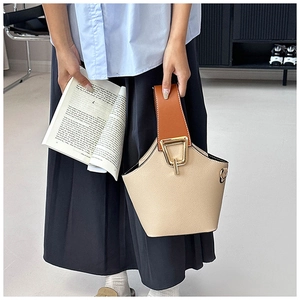 Dettaglio della borsa a secchiello beige con manico in pelle marrone e chiusura dorata