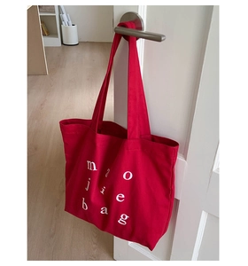 Detail of red canvas tote bag with white letter print hanging on a white door