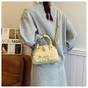 Detail of light yellow shell bag with lace bow and plaid ribbon on a model