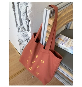 Detail of brick red canvas tote bag with yellow letters hanging on a chair