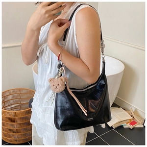 Chic black crocodile embossed crescent bag with plush bear charm worn by a model
