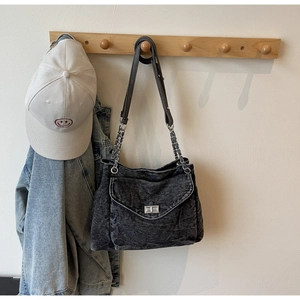 Detail of black washed denim shoulder bag featuring a silver metal twist lock closure