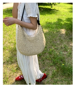 Detail of a beige woven hobo bag with black leather strap on a summer outdoor background