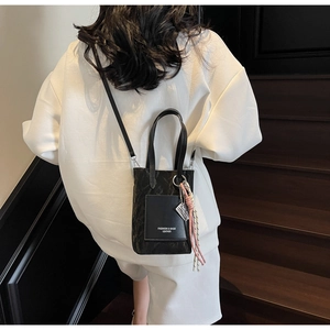 Détail du sac en cuir noir texturé avec texte imprimé et charm à pompon élégant
