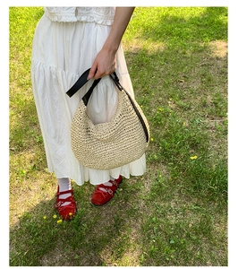 Detail of a cream woven straw hobo bag with an adjustable black leather shoulder strap