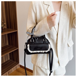 Detail of black pebbled leather shell bag with lace bow and plaid ribbon on a model