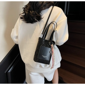 Détail du sac seau noir matelassé avec pendentif tissé et logo de mode en relief
